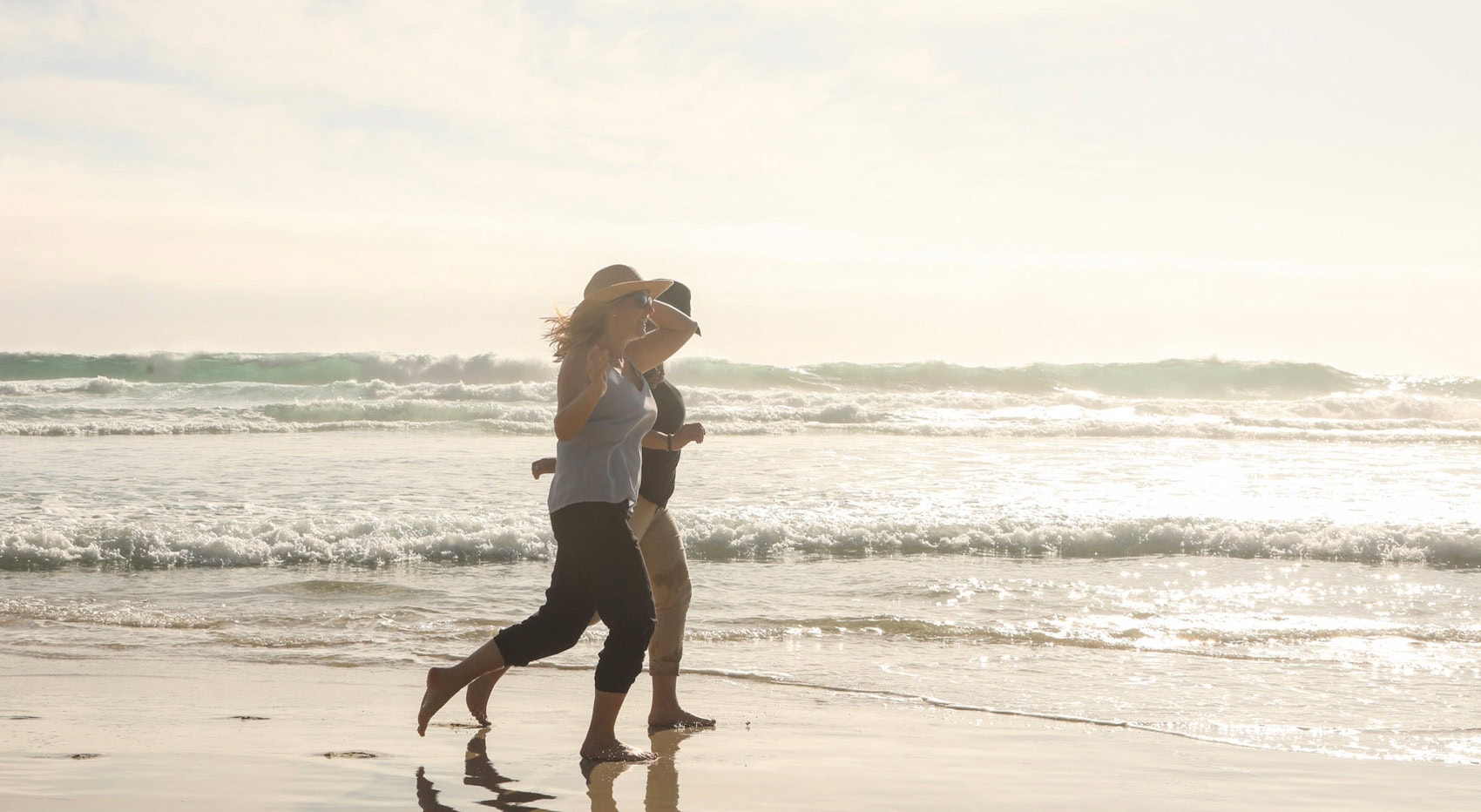 Zwei Damen laufen barfuß am Strand in Südafrika. 