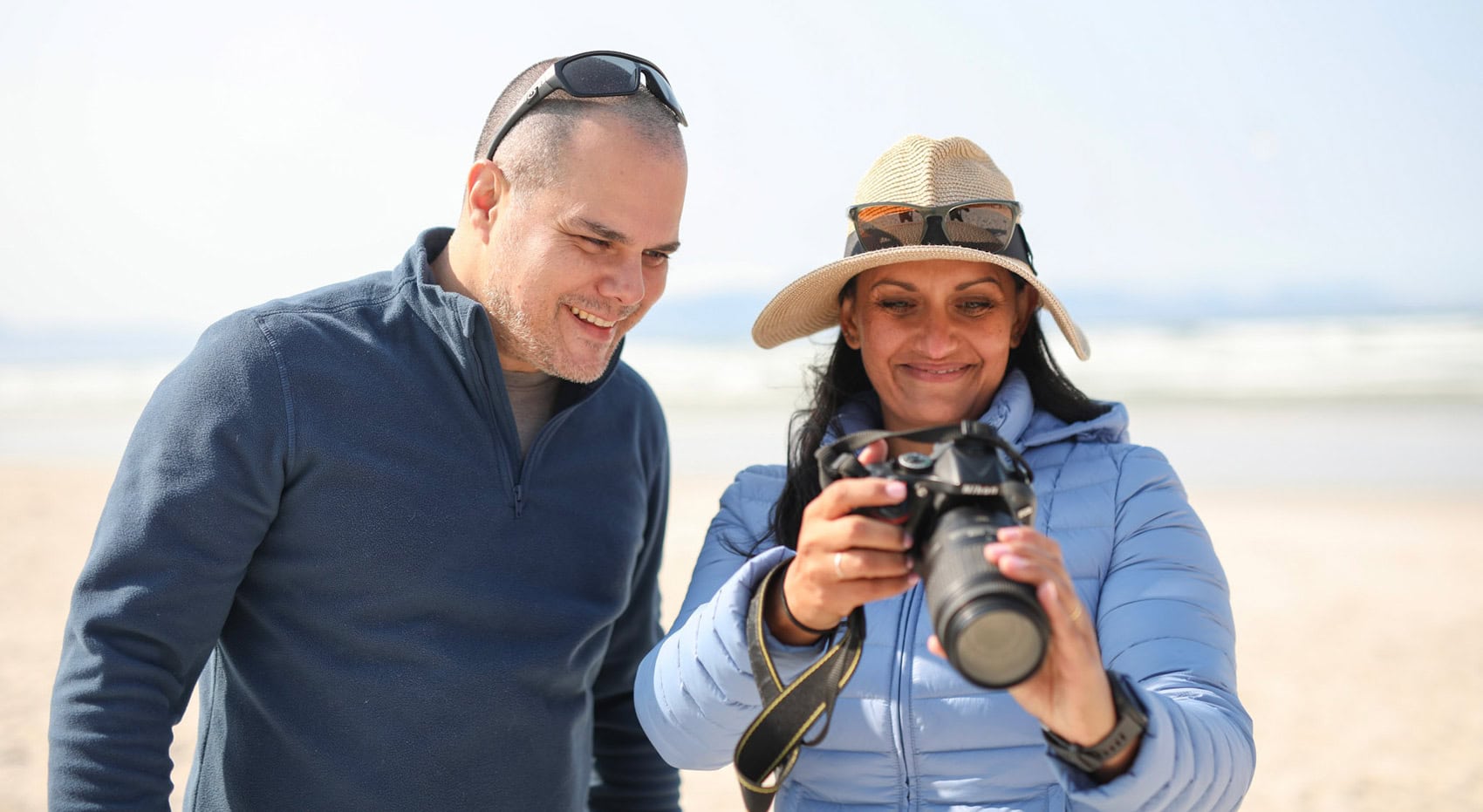 Gäste betrachten ihr Foto auf einer Spiegelreflexkamera am Strand entlang der Garden Route.