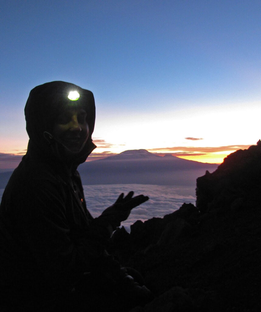 Ein Trekking-Gast bei der Besteigung des Mt Meru mit Blick auf den Kilimandscharo in den frühen Morgenstunden.