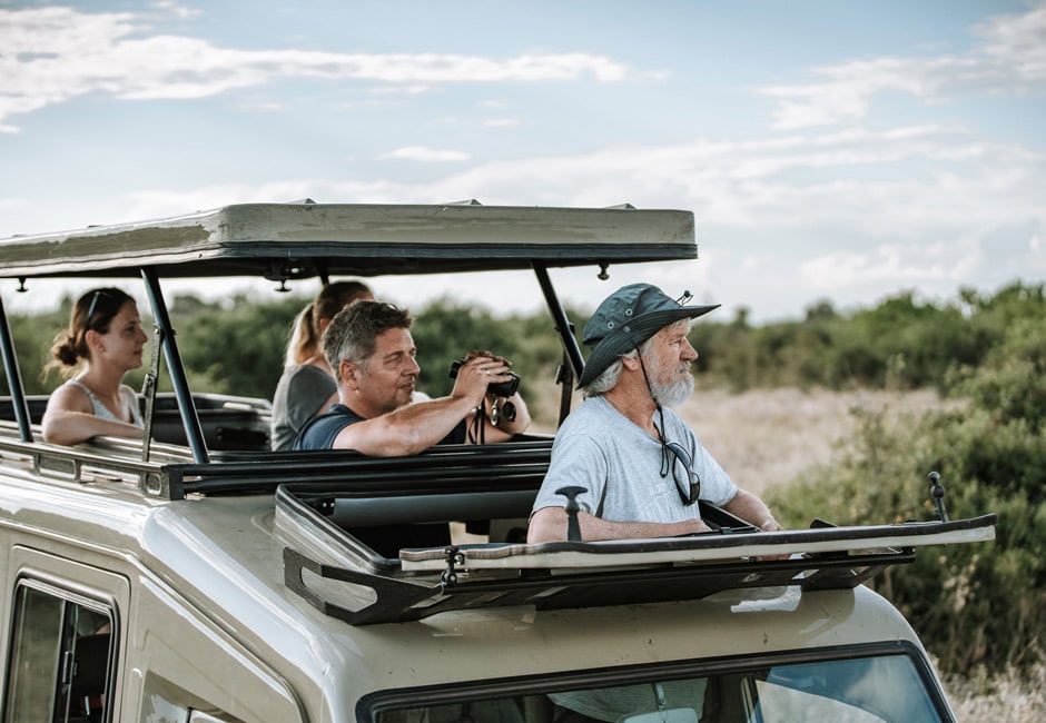 Gäste in einem Safarifahrzeug, schauen aus der Dachluke in die Wildnis.