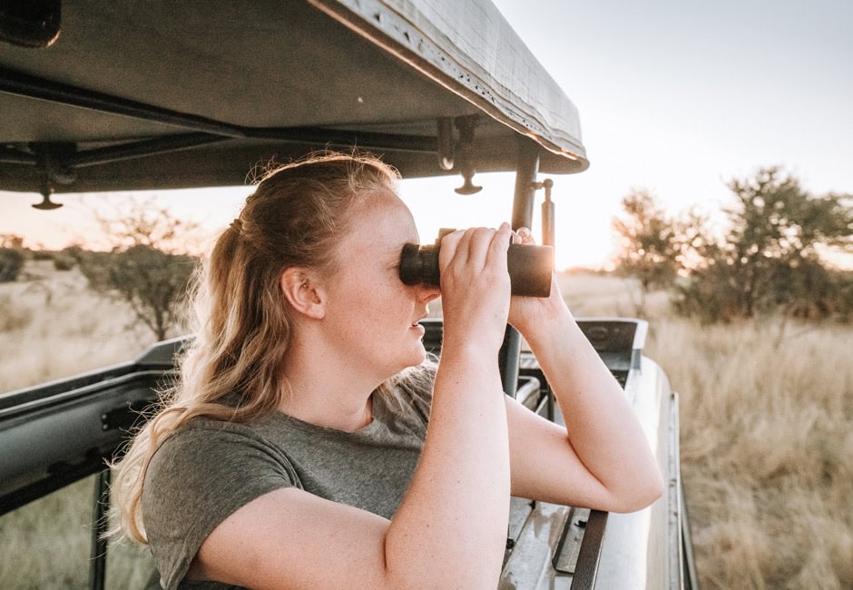 Ein Gast bei einer Afrika Rundreise in 3 Wochen, mit Fernglas im Safarifahrzeug.