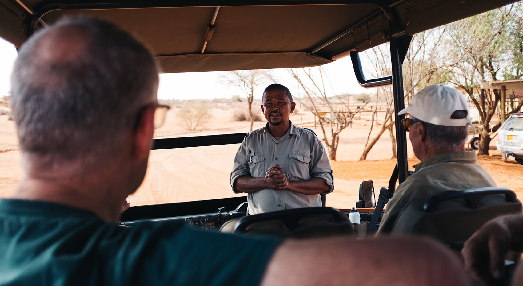 Ein Guide erklärt einer Reisegruppe etwas, während alle gemeinsam im Safariauto sitzen. Ein Guide erklärt einer Reisegruppe etwas, während alle gemeinsam im Safariauto sitzen.