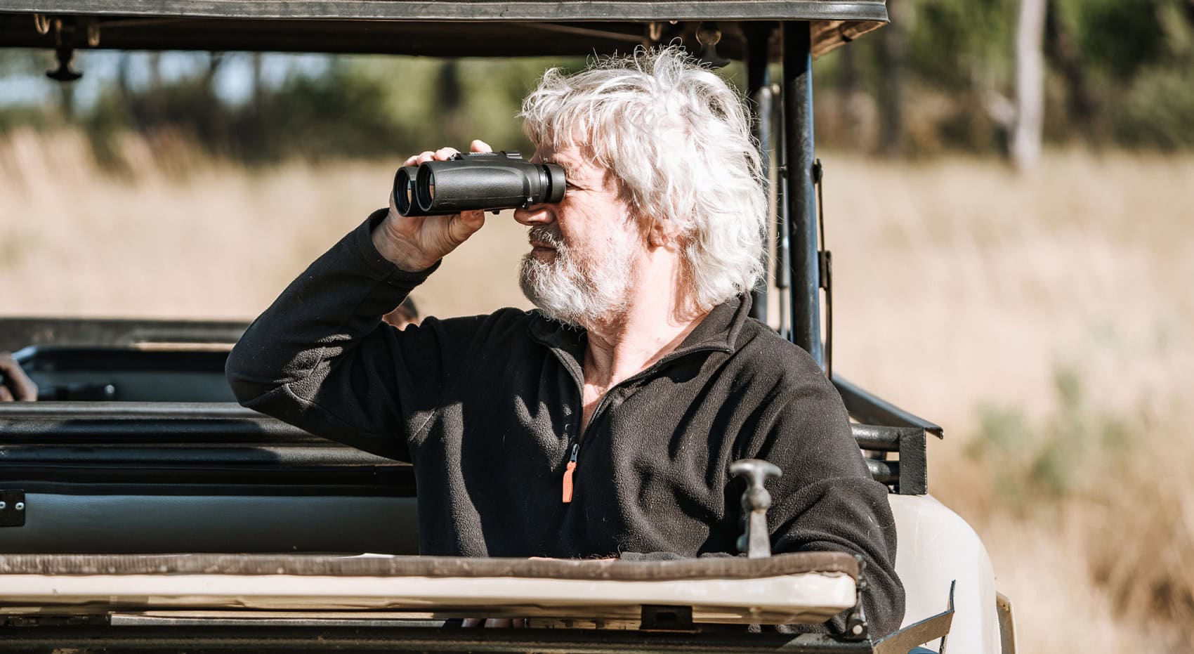 Ein Mann schaut durch ein Fernglas aus der Dachluke eines Safari-Fahrzeuges. Ein Mann schaut durch ein Fernglas aus der Dachluke eines Safari-Fahrzeuges.