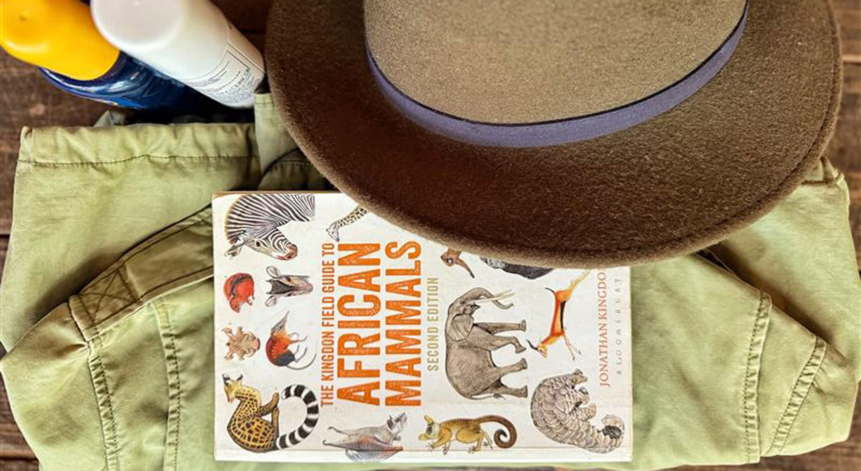 Ein African Mammals Buch auf einen Safari-Jacke, neben Hut, Sonnencreme und Mückenspray. Ein African Mammals Buch auf einen Safari-Jacke, neben Hut, Sonnencreme und Mückenspray.